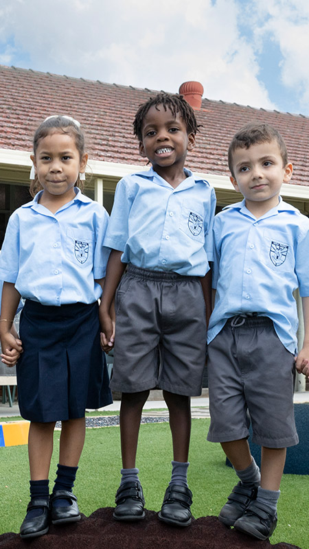 Three kindergarten students at Holy Family Primary, East Granville standing atop playground equipment