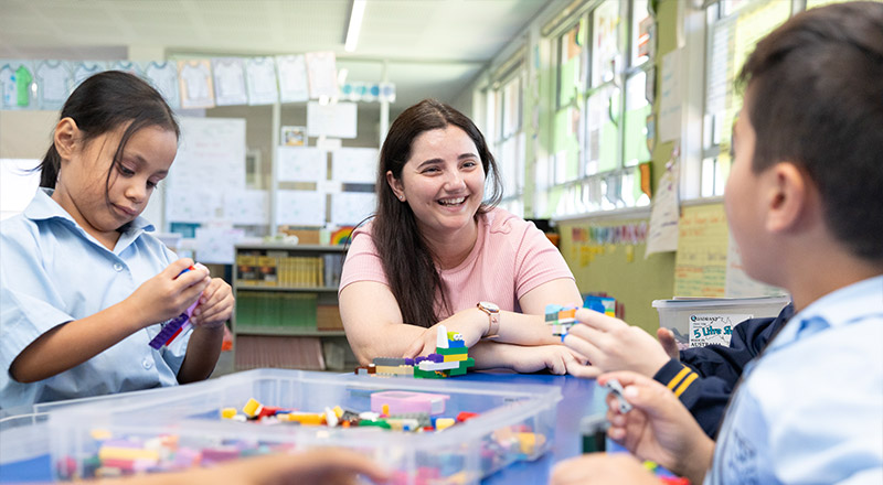 Teacher from Holy Family Primary, East Granville sitting with students at desk