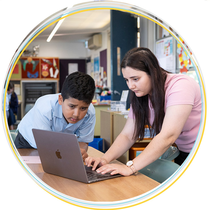 Holy Family Primary, East Granville assisting a student. They are working from a Macbook